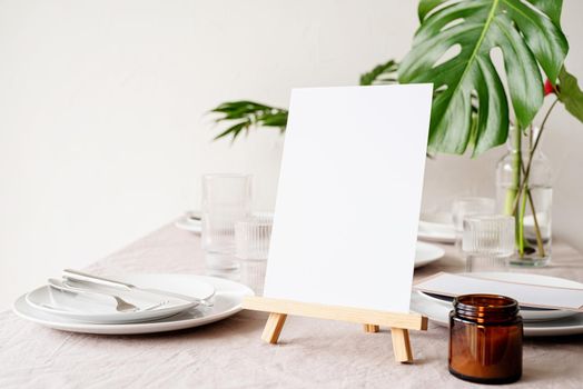 Mock up label the blank menu frame in bar restaurant, Stand for booklets with white paper, wooden tent card on restaurant table with tropical bouquet