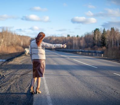 The girl stops the car on the highway with her hand. Stylish woman on the road stops the car go on a journey. A road in the middle of the forest.