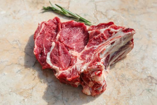 A fresh piece of beef with ribs, ready to roast. Nearby are the spices of rosemary. On a stone cutting board