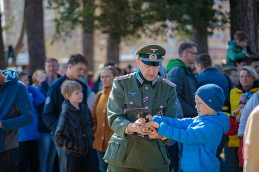 Reconstruction of the Second World War. A man in the uniform of a German officer shows a boy how to shoot a pistol. The Great Patriotic War. Liberation of Odessa. Zelenograd Russia April 18, 2021