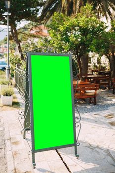 Wooden easel in a beautiful forged metal frame with an empty field stands in front of the entrance to the restaurant. High quality photo