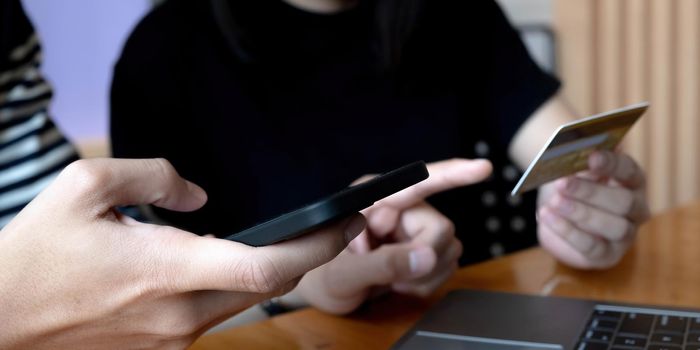 Selective focus of positive man holding smartphone while using credit card near woman.