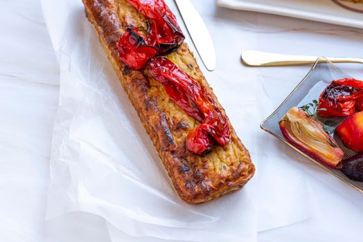 Homemade healthy salted cake with vegetables and roasted red peppers on top. Rectangular shapes on a white marble background. Glass saucers, gold cutlery, and a towel. High quality photo, top view