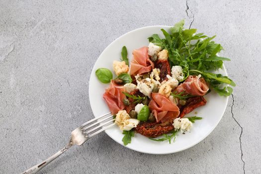 Salad arugula, Parma ham with sun-dried tomatoes, mozzarella slices, croutons, capers, seasoned oil and spices