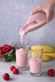 Pour freshly prepared banana-strawberry smoothie from a bottle into glasses