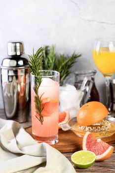 Gin cocktail with rosemary and pomegranate on a table among citrus fruits and drinks.