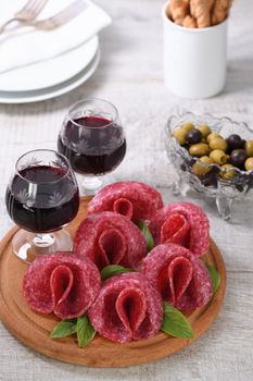 light meal snack from salami folded in the form of a flower with a glass sherry on a wooden dish. Close-up.