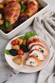 Sliced ​​chicken breast stuffed with goat cheese with spinach, wrapped in prosciutto, with a side dish of baked potatoes, tomato and dried prunes