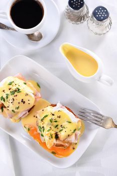 Hollandaise butter sauce in a gravy boat for breakfast served with Eggs Benedict- fried English bun, ham, poached eggs, a cup of coffee