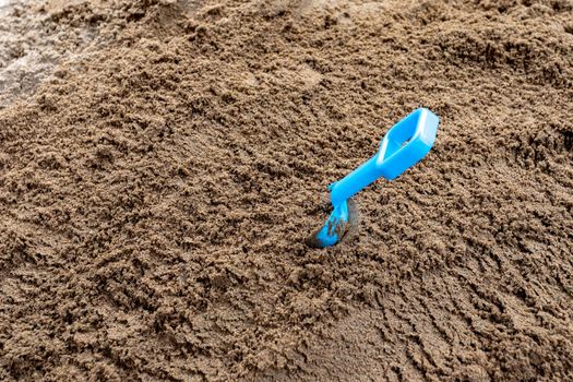 A blue plastic shovel sticks out of play sand in a sandbox.