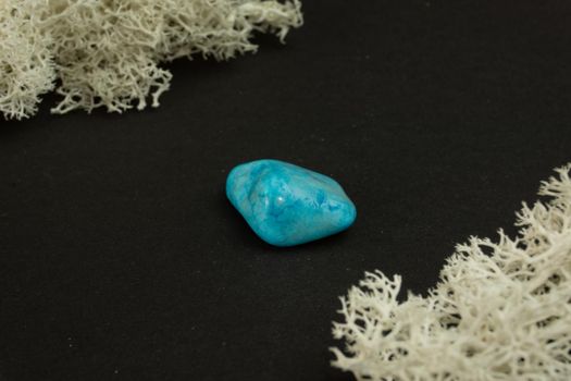 Howlite or turquoise imitation from Republic of South Africa RSA. Natural mineral stone on a black background surrounded by moss. Mineralogy, geology, magic, semi-precious stones and samples of minerals