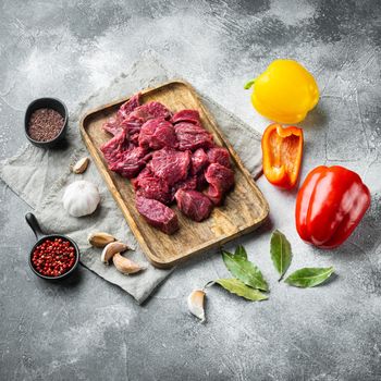 Fresh beef chunks served on table with ingredients ready for cooking set with sweet bell pepper, on gray stone background, square format