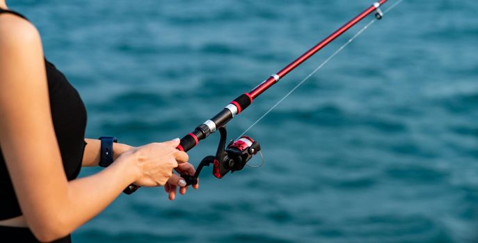 Woman hand holding fishing rod with sea background, fishing at sunset.