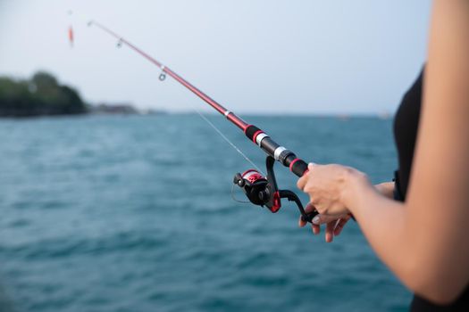 Woman hand holding fishing rod with sea background, fishing at sunset.