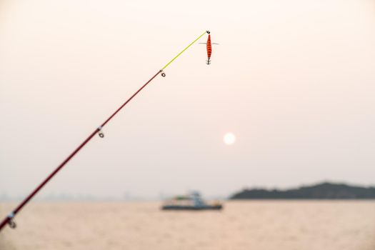 Artificial small fish on a fishing rod with sea background, fishing at sunset.