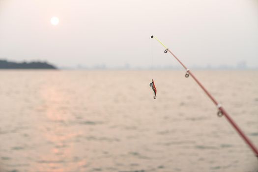 Artificial small fish on a fishing rod with sea background, fishing at sunset.