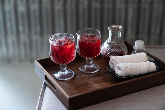Welcome drink red mocktail and white towel served on wooden tray.