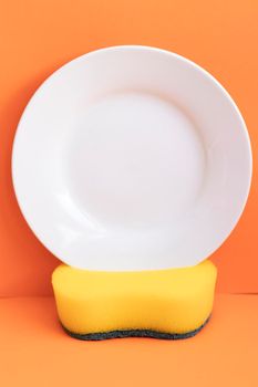 Yellow sponge next to white plate with orange background