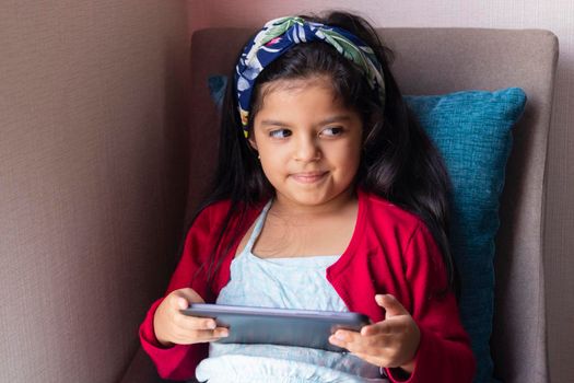 Little girl sitting is playing with her tablet at home