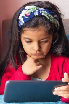 Little girl sitting is playing with her tablet at home