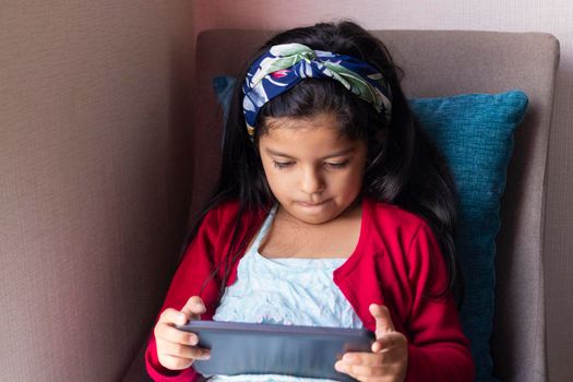 Little girl sitting is playing with her tablet at home