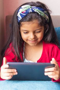 Little girl sitting is playing with her tablet at home