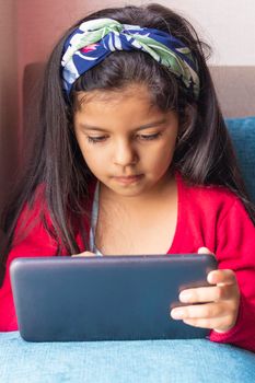 Little girl sitting is playing with her tablet at home