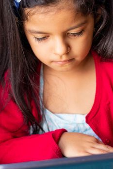 Little girl sitting is playing with her tablet at home