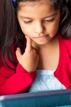 Little girl sitting is playing with her tablet at home