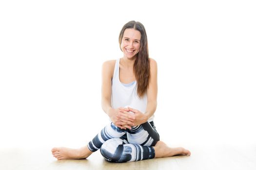 Young sporty female yoga instructor in bright white yoga studio, smiling cheerfully, looking at the camera