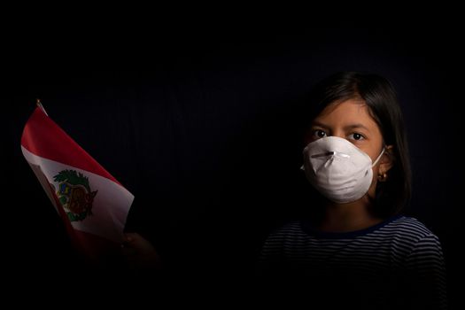 Portrait of little Peruvian girl wearing medical mask and holding hopefully the flag of Peru