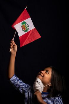 Portrait of little Peruvian girl wearing medical mask and holding hopefully the flag of Peru