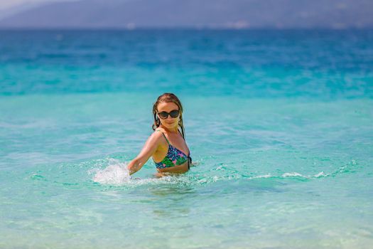 Young beautiful girl splashes in the blue water of the ocean. Rejoices and laughs on vacation
