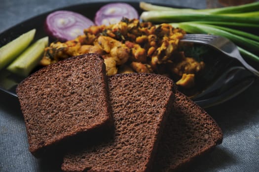 Chicken dish, black bread, onions and cucumbers on a dark background.