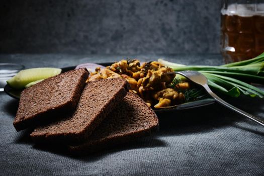 Chicken dish, black bread, onions and cucumbers on a dark background.