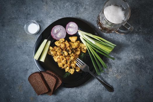 Chicken dish, black bread, onions and cucumbers on a dark background.