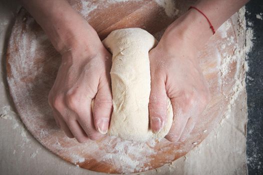 Women's hands knead the dough from wheat flour