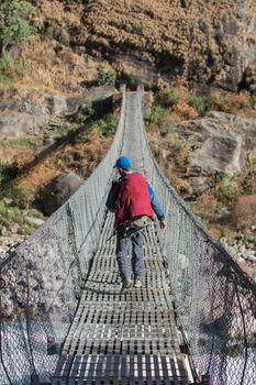 Adventurer trekking across a suspension bridge hanging over Marshyangdi river, Annapurna circuit, Nepal