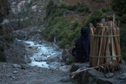 Strong working nepalese woman resting, sitting, looking at Marshyangdi river underneath her, Annapurna circuit, Himalaya, Nepal, Asia