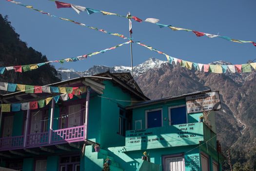 Turquoise tea house with buddhist prayer flags underneath snow covered peak along Annapurna circuit, Himalaya, Nepal, Asia