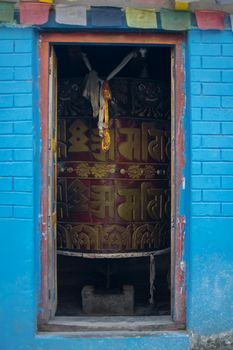 Huge tibetan prayer wheel inside a house with hanging buddhist prayer flags