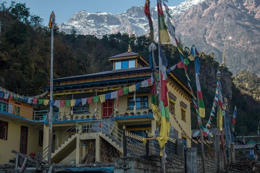 Yellow buddhist monastery with buddhist prayer flags, underneath himalayan mountains along Annapurna circuit