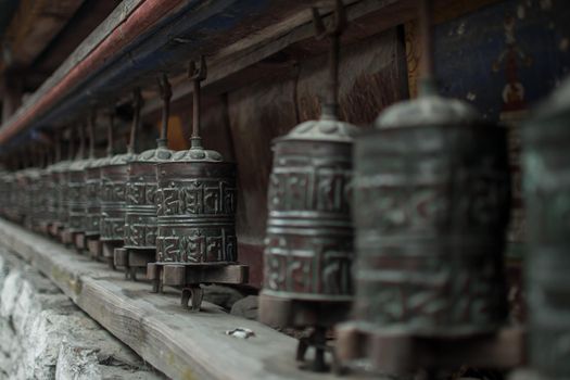 Buddhist prayer wheels in a long row with nepalese mantra text