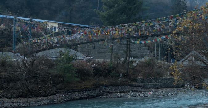 Panorama of Chame suspension bridge colorful buddhist prayer flags over Marshyangdi river, Annapurna circuit, Nepal