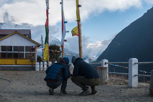 Two friends crouching by colorful buddhist prayer flags in the mountains