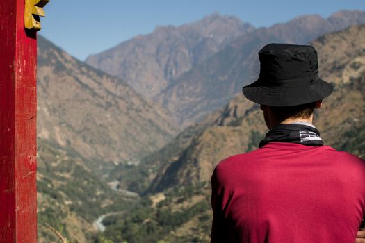 Man hiking in Nepal, looking out over a river and the mountains