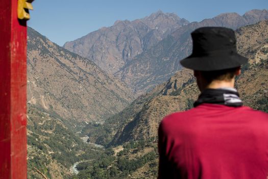 Man hiking in Nepal, looking out over a river and the mountains