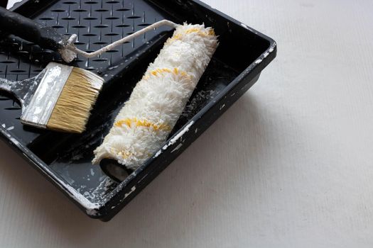 In a black tray on a white background are a brush and a roller for painting the walls. Repair concept.
