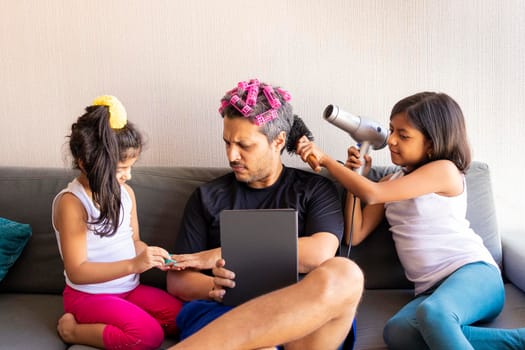 Pretty daughters are painting the nails and combing the hair of their handsome young father