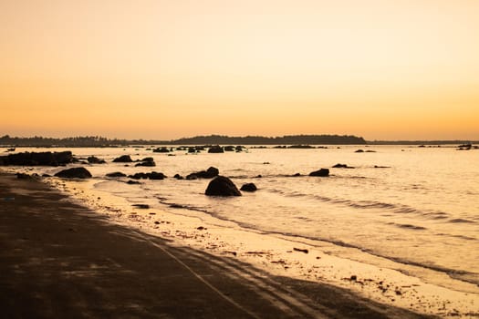 A bright golden orange sunset over a beach with rocks in the water waves near Ngwesaung beach, Irrawaddy, western Myanmar